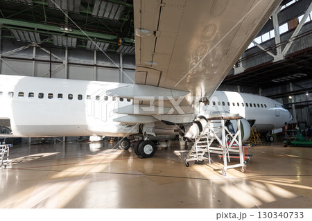 White passenger airplane in the aircraft hangar. Checking mechanical systems for flight operations. Plane under maintenance 130340733