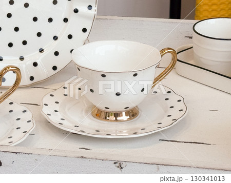 White ceramic cup with golden handle and black polka dots on saucer. Home decor, kitchenware, and stylish tableware design. 130341013