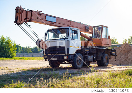 Old mobile crane on a construction site against the background of a fence and a pile of sand after work. Old mobile crane on a construction site against the background of a fence and a pile of sand after work. 130341078
