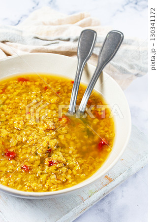 Delicious bowl of golden lentil soup with spices and red pepper flakes presented on a rustic wooden surface Delicious bowl of golden lentil soup with spices and red pepper flakes presented on a rustic wooden surface 130341172