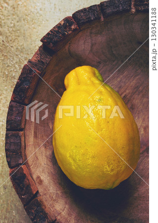 Bright yellow lemon resting in a rustic wooden bowl on a textured surface, creating a natural and fresh aesthetic Bright yellow lemon resting in a rustic wooden bowl on a textured surface, creating a natural and fresh aesthetic 130341188
