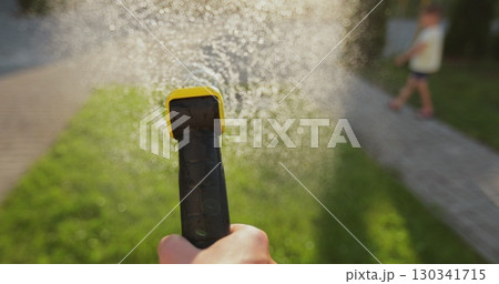 Man hand watering green lawn near the house, man's hand holding the water hose against green lawn. Man hand watering green lawn near the house, man's hand holding the water hose against green lawn. 130341715
