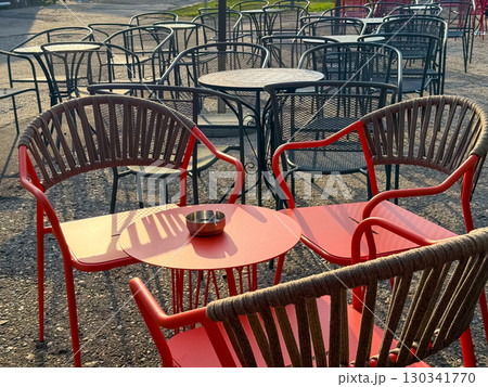Red plastic chairs and a checkered table on an outdoor cafe terrace. Street dining, casual atmosphere and everyday urban lifestyle. Red plastic chairs and a checkered table on an outdoor cafe terrace. Street dining, casual atmosphere and everyday urban lifestyle. 130341770