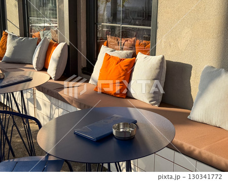 Outdoor cafe with benches, pillows, and menus placed on blue round tables. Hospitality, design, and urban lifestyle reflected in dining, leisure, and social culture. 130341772