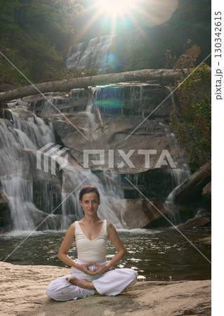 Young woman sitting in lotus pose under tropical waterfall meditating with calm strength and mindfulness fully connected to nature energy tranquility and inner balance Young woman sitting in lotus pose under tropical waterfall meditating with calm strength and mindfulness fully connected to nature energy tranquility and inner balance 130342615