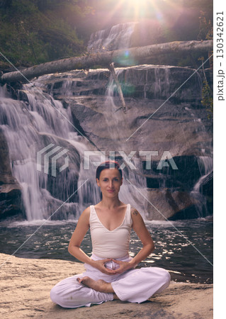 Young woman sitting in lotus pose under tropical waterfall meditating with calm strength and mindfulness fully connected to nature energy tranquility and inner balance Young woman sitting in lotus pose under tropical waterfall meditating with calm strength and mindfulness fully connected to nature energy tranquility and inner balance 130342621