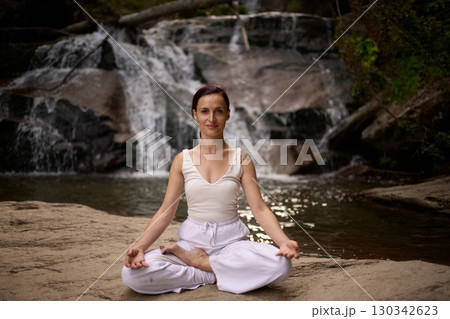 Young woman sitting in lotus pose under tropical waterfall meditating with calm strength and mindfulness fully connected to nature energy tranquility and inner balance Young woman sitting in lotus pose under tropical waterfall meditating with calm strength and mindfulness fully connected to nature energy tranquility and inner balance 130342623