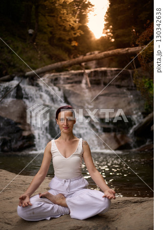 Young woman sitting in lotus pose under tropical waterfall meditating with calm strength and mindfulness fully connected to nature energy tranquility and inner balance Young woman sitting in lotus pose under tropical waterfall meditating with calm strength and mindfulness fully connected to nature energy tranquility and inner balance 130342638