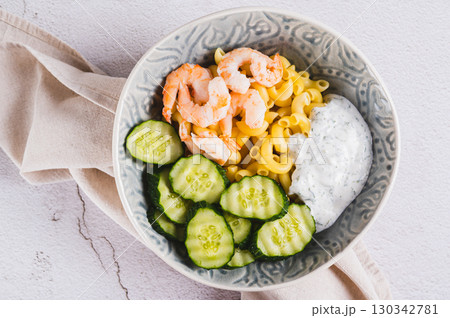 Close up of bowl with pasta, shrimp, cucumber and sauce on the table top view 130342781