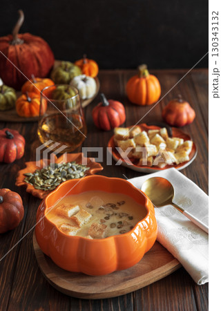 Creamy pumpkin soup with croutons and seeds, served in a pumpkin-shaped bowl on dark wooden table. Creamy pumpkin soup with croutons and seeds, served in a pumpkin-shaped bowl on dark wooden table. 130343132