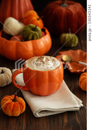 Cozy pumpkin latte in a pumpkin-shaped mug with whipped cream and spices, surrounded by autumn decor. 130343141