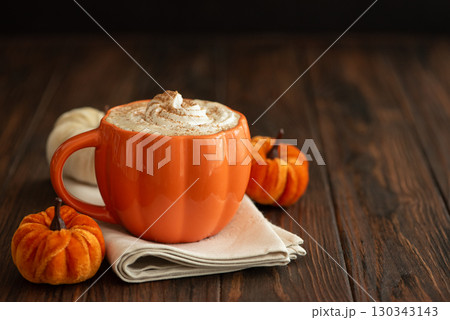 Cozy pumpkin latte in a pumpkin-shaped mug with whipped cream and spices, surrounded by autumn decor. Cozy pumpkin latte in a pumpkin-shaped mug with whipped cream and spices, surrounded by autumn decor. 130343143