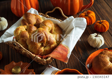 Autumnal tea set with baked buns into basket, pumpkin-shaped teapot and mug on a wooden table. Autumnal tea set with baked buns into basket, pumpkin-shaped teapot and mug on a wooden table. 130343147