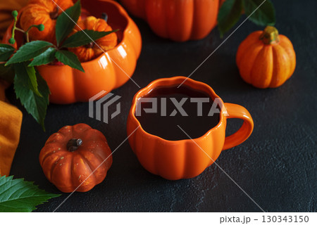 Autumnal tea set with pumpkin-shaped teapot and mug, and decorative pumpkins on a black wooden table. Autumnal tea set with pumpkin-shaped teapot and mug, and decorative pumpkins on a black wooden table. 130343150