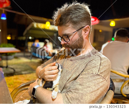 Man looking at kitten with mutual gaze in close moment. Intimacy, trust, and human animal connection with companionship, affection, and emotional bond 130343323