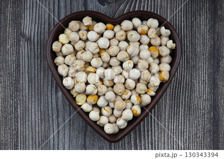Roasted white chickpeas in wooden bowl on wooden background, top view. White chickpeas, with their high fiber content, are very healthy to consume. 130343394