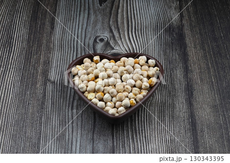 Roasted white chickpeas in wooden bowl on wooden background, top view. White chickpeas, with their high fiber content, are very healthy to consume. 130343395