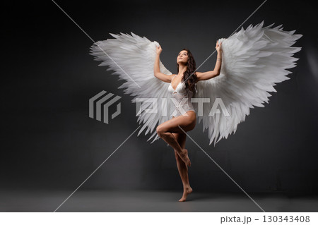 Woman with angel wings gracefully poses under colorful light projection Woman with angel wings gracefully poses under colorful light projection 130343408