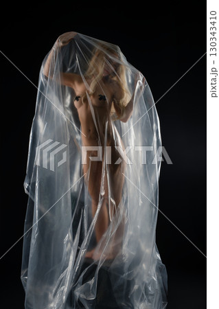 Studio portrait of a blonde woman artistically draped in transparent material Studio portrait of a blonde woman artistically draped in transparent material 130343410