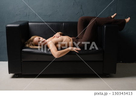 Blonde woman poses gracefully in a studio setting on a black couch 130343413