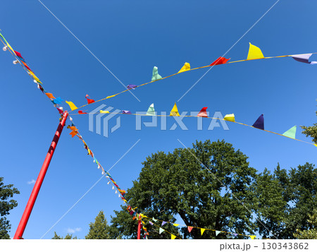 Colorful festive pennant flags stretched on strings between red poles against clear blue summer sky creating bright decorative background for holiday celebration and cheerful events 130343862