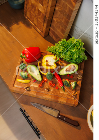 Colorful fresh vegetables and avocado on a wooden board in cozy kitchen setting Colorful fresh vegetables and avocado on a wooden board in cozy kitchen setting 130344344