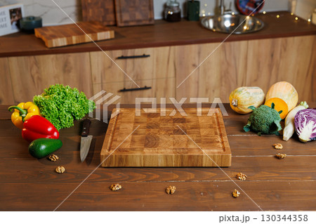 Rustic wooden cutting board with fresh vegetables on wooden table in cozy kitchen 130344358