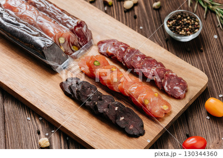 Assorted gourmet sausages sliced and vacuum packed on rustic wooden background with spices Assorted gourmet sausages sliced and vacuum packed on rustic wooden background with spices 130344360
