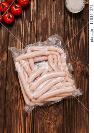 Vacuum packed chicken sausages on wooden table with tomatoes and salt in background Vacuum packed chicken sausages on wooden table with tomatoes and salt in background 130344375