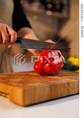 Cutting fresh red bell pepper on a wooden board in cozy kitchen interior Cutting fresh red bell pepper on a wooden board in cozy kitchen interior 130344389