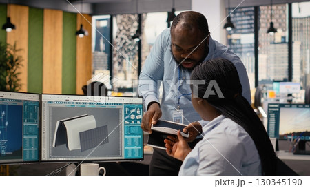 Technicians work together to evaluate advanced solar cell technology clean energy based device. Research and development office workers test solar panel lamp prototype, checking power output, camera B 130345190