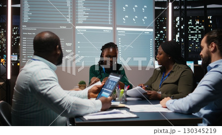 Close up of diverse business staff exchanging reports files and insights to forecast company objectives in a quiet strategy room after hours at night. Finance projections collaboration. Camera A. 130345219