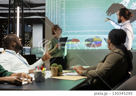 Diverse group of corporate associates look into project timelines and agenda, creating a strategy for development after hours in conference room. Goal setting in a business environment. 130345295