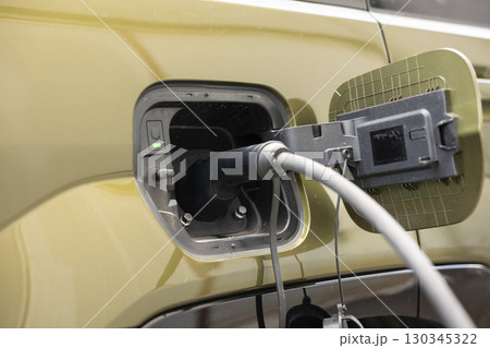 Close up of eco conscious electric car with charging port flap opened to recharge battery. Electric cable connector inserted into EV vehicle, transition to renewable energy concept Close up of eco conscious electric car with charging port flap opened to recharge battery. Electric cable connector inserted into EV vehicle, transition to renewable energy concept 130345322