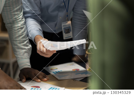 Close up of colleagues attend an after hours business meeting for analysis on files, exchange infographics and performance indicators to ensure project agenda planning. Late night briefing. Close up of colleagues attend an after hours business meeting for analysis on files, exchange infographics and performance indicators to ensure project agenda planning. Late night briefing. 130345329