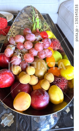 Mix of fresh tropical fruits fills silver bowl with grapes, strawberries, and kiwi, creating vibrant tropical fruits display on glass topped table, radiating freshness and tropical fruits charm. Mix of fresh tropical fruits fills silver bowl with grapes, strawberries, and kiwi, creating vibrant tropical fruits display on glass topped table, radiating freshness and tropical fruits charm. 130345838