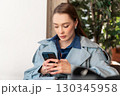 Young woman in trench coat using smartphone while 130345958