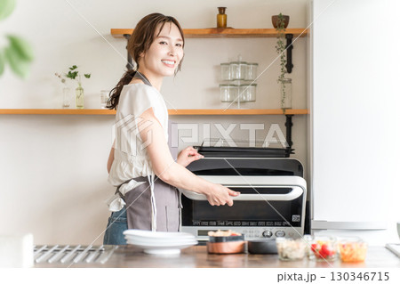 キッチンで電子レンジを使う女性（笑顔） 130346715