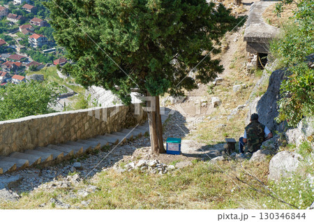 コトルの山に登る途中にある木の下で休憩する男性 130346844