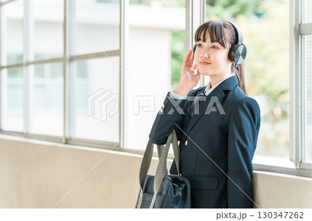 学校の廊下でヘッドフォンで音楽を聴く制服姿の小学生,中学生,高校生の女の子 130347262