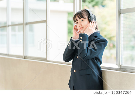 学校の廊下でヘッドフォンで音楽を聴く制服姿の小学生,中学生,高校生の女の子 130347264