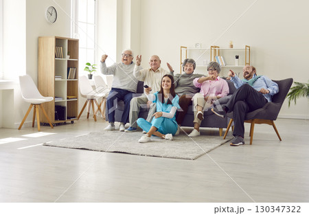 Group of senior people watching TV in retirement home with young nurse holding remote. Group of senior people watching TV in retirement home with young nurse holding remote. 130347322