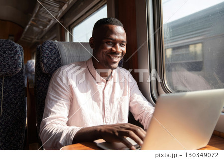 Smiling african american businessman in shirt using laptop for work in modern train, business trip concept 130349072