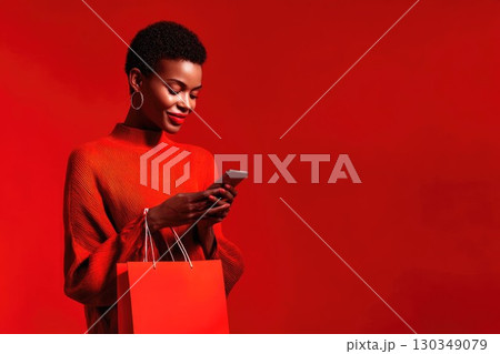 Beautiful smiling African woman with short hair holding shopping bag and using smartphone for online shopping. Sale and discount season concept, banner with fashionable woman and copy space Beautiful smiling African woman with short hair holding shopping bag and using smartphone for online shopping. Sale and discount season concept, banner with fashionable woman and copy space 130349079