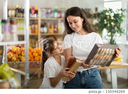 Mother consults with her daughter about which sweets to buy in the grocery section of supermarket - nougat or cookies Mother consults with her daughter about which sweets to buy in the grocery section of supermarket - nougat or cookies 130349269
