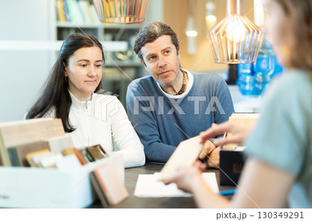 Married couple discusses choice of material - laminate or wood - for their future furniture with furniture store manager 130349291