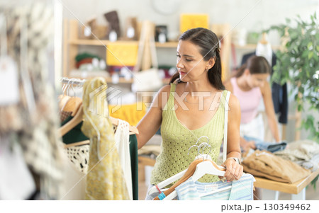 Happy middle-aged woman choosing something for summer in clothing store Happy middle-aged woman choosing something for summer in clothing store 130349462
