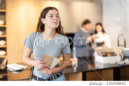 Female buyer with samples of material chooses kitchen set in furniture store Female buyer with samples of material chooses kitchen set in furniture store 130349641