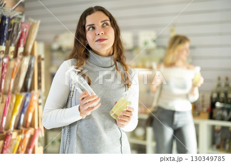 Girl sniffs fragrance of perfume, chooses scent spray, woman shopping in background 130349785