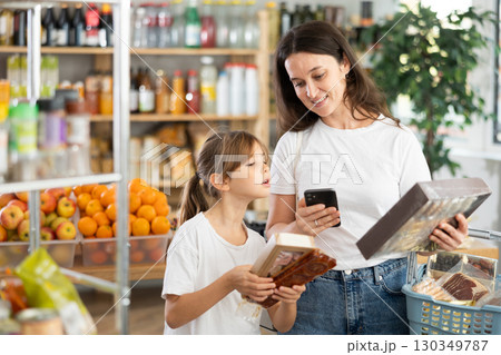 Daughter and mother choose delicious cookies in supermarket - scan QR code on label with smartphone Daughter and mother choose delicious cookies in supermarket - scan QR code on label with smartphone 130349787